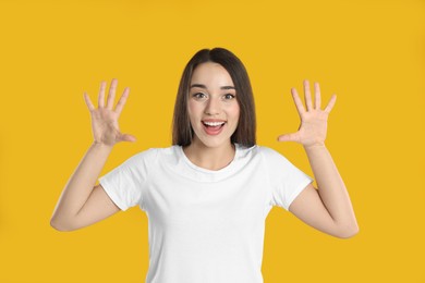 Photo of Woman in white t-shirt showing number ten with her hands on yellow background