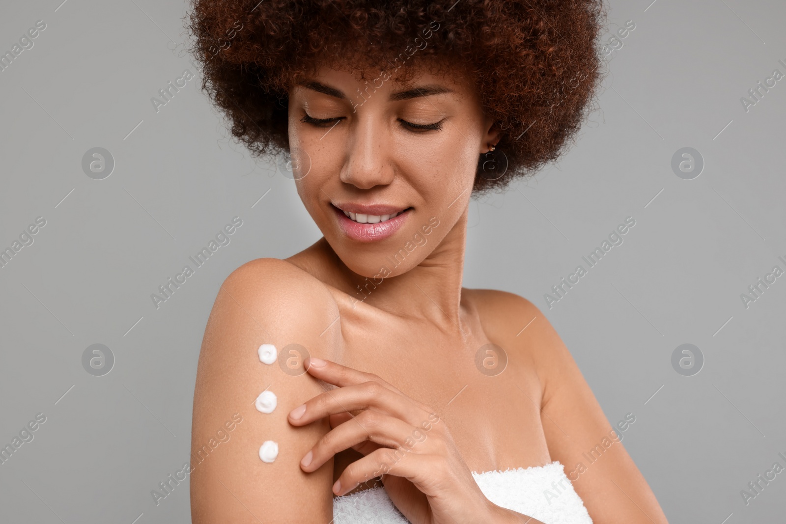 Photo of Beautiful young woman applying body cream onto arm on grey background