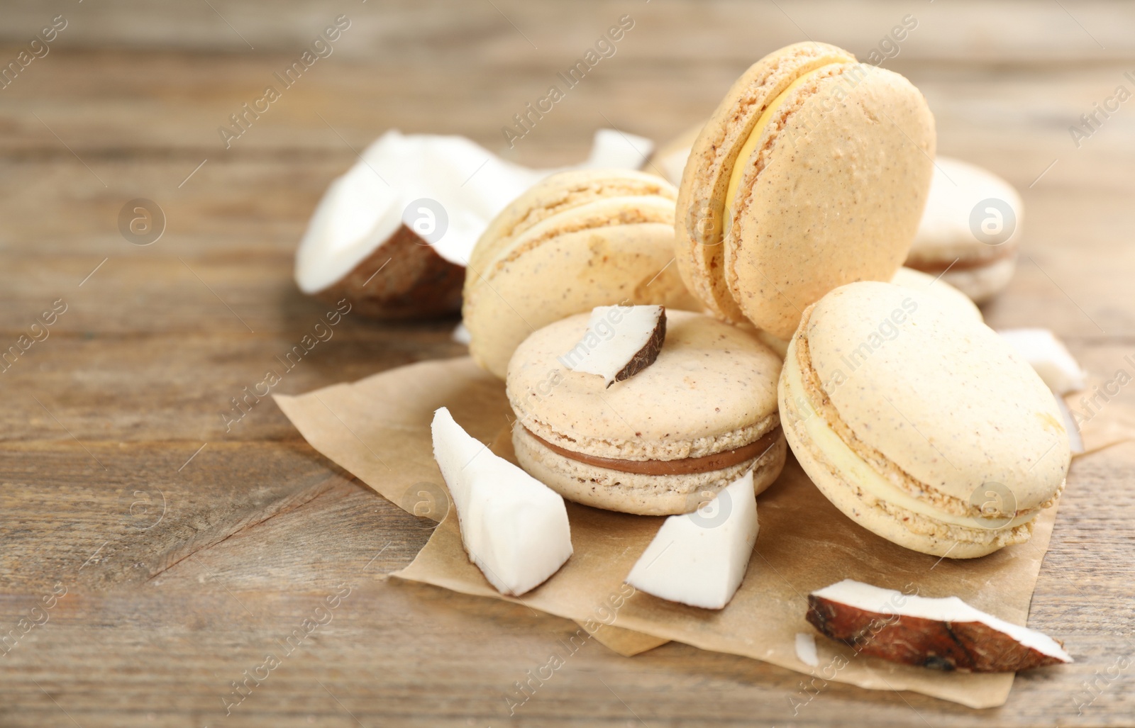 Photo of Delicious macarons and pieces of coconut on wooden table. Space for text