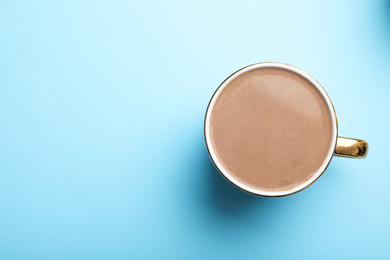 Delicious cocoa drink in cup on light blue background, top view. Space for text