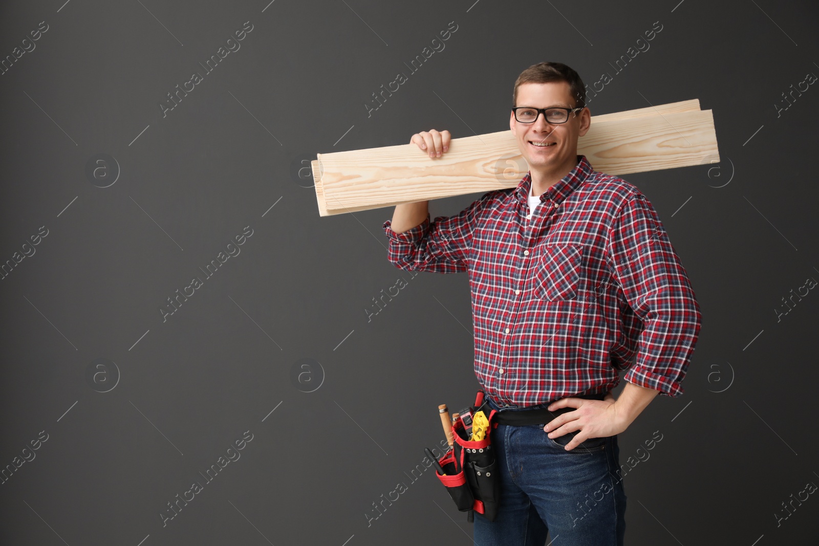 Photo of Handsome carpenter with wooden planks on dark background. Space for text