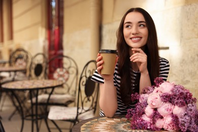 Beautiful woman with bouquet of spring flowers and coffee in outdoor cafe, space for text