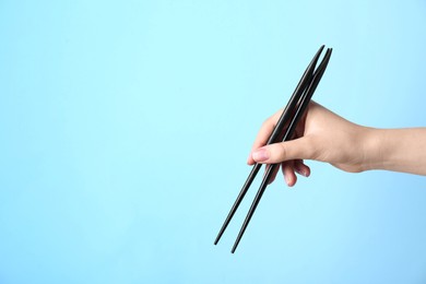 Photo of Woman holding pair of black chopsticks on light blue background, closeup. Space for text