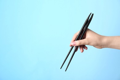 Woman holding pair of black chopsticks on light blue background, closeup. Space for text