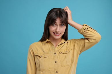 Photo of Embarrassed woman scratching head on light blue background