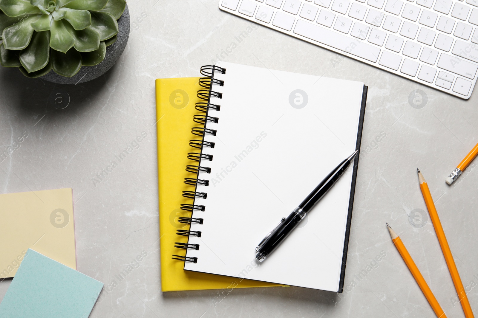 Photo of Open blank notebook, keyboard and stationery on light grey marble table, flat lay