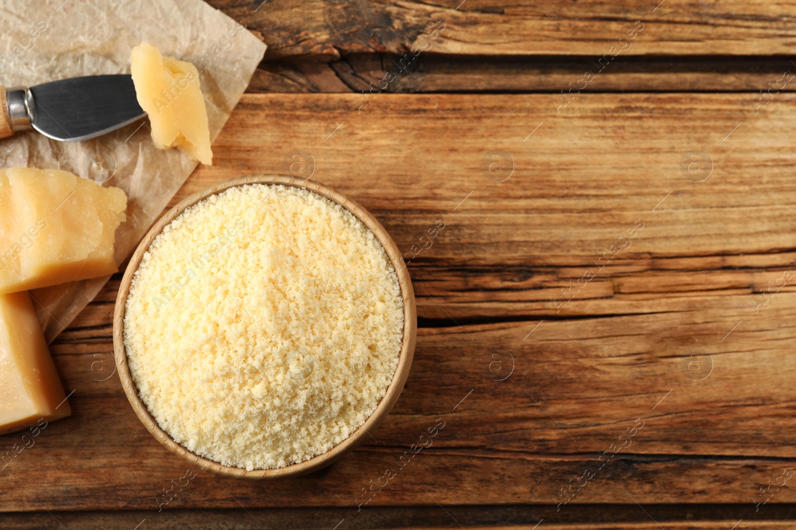 Photo of Bowl with grated parmesan cheese on wooden table, flat lay. Space for text