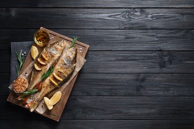 Tasty homemade roasted perches on black wooden table, top view and space for text. River fish