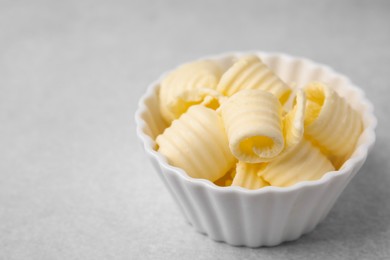 Photo of Tasty butter curls in bowl on light grey table, closeup. Space for text