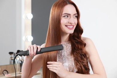 Beautiful woman using hair iron in room