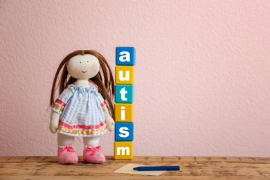 Doll and cubes with word "Autism" on table