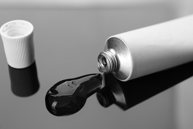 Photo of Open white tube with ointment on dark mirror surface, closeup