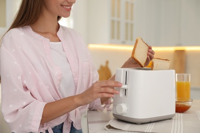 Young woman using toaster at table in kitchen, closeup