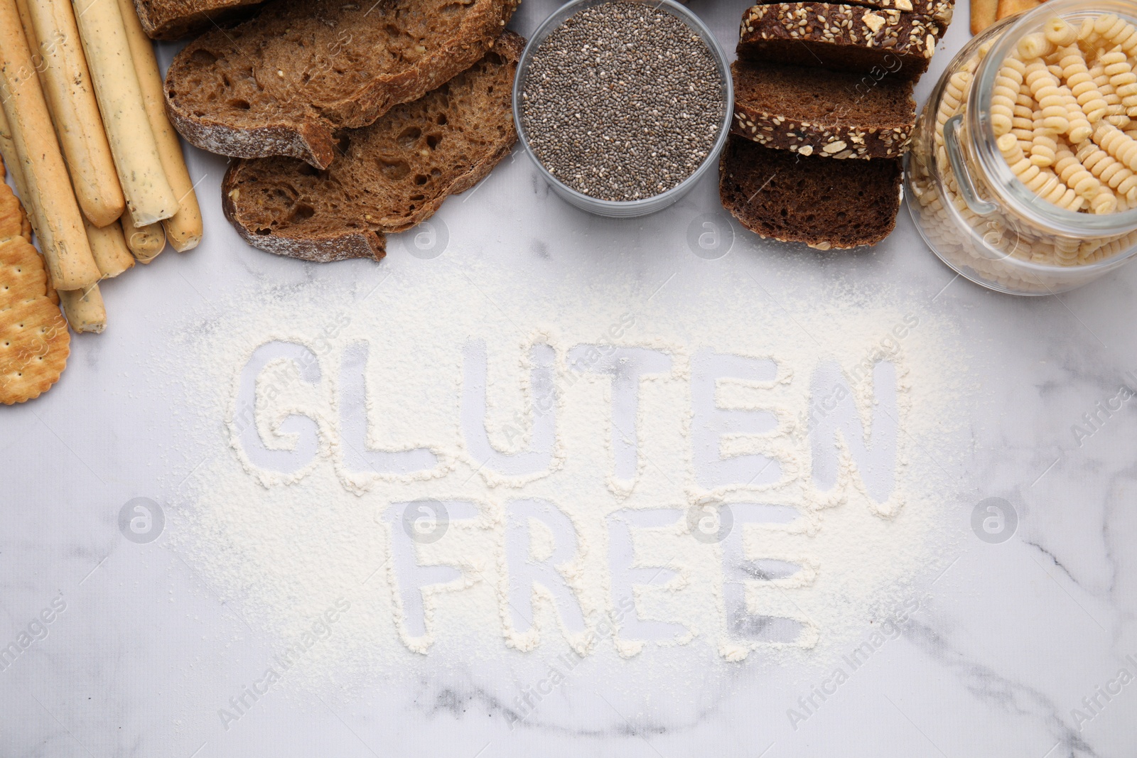 Photo of Different healthy products and phrase Gluten Free made of flour on white marble table, flat lay