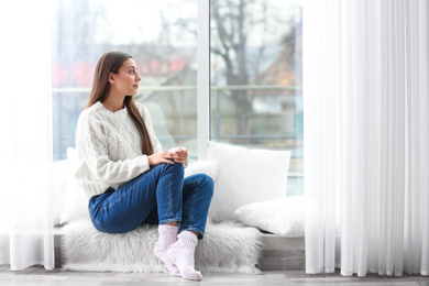 Young woman in sweater sitting near window indoors