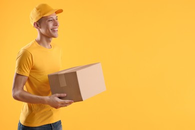 Photo of Happy courier with parcel on orange background. Space for text