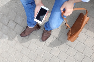 Photo of Man in stylish leather shoes using mobile phone outdoors, closeup