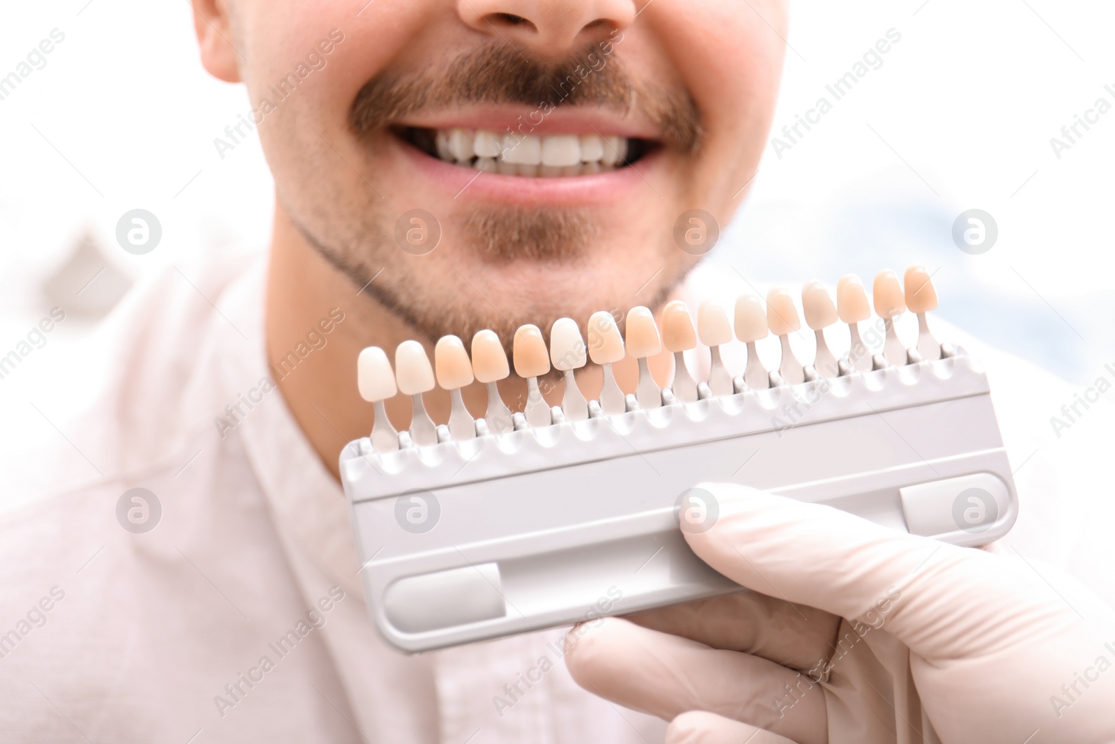 Photo of Dentist checking young man's teeth color, closeup