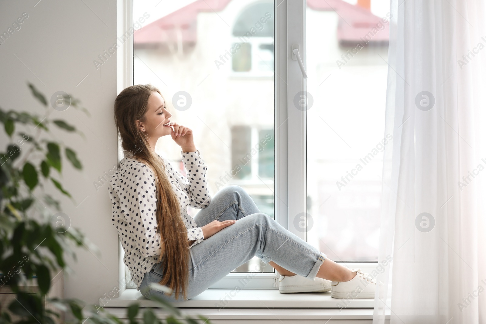 Photo of Beautiful young woman on windowsill at home