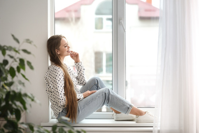 Beautiful young woman on windowsill at home