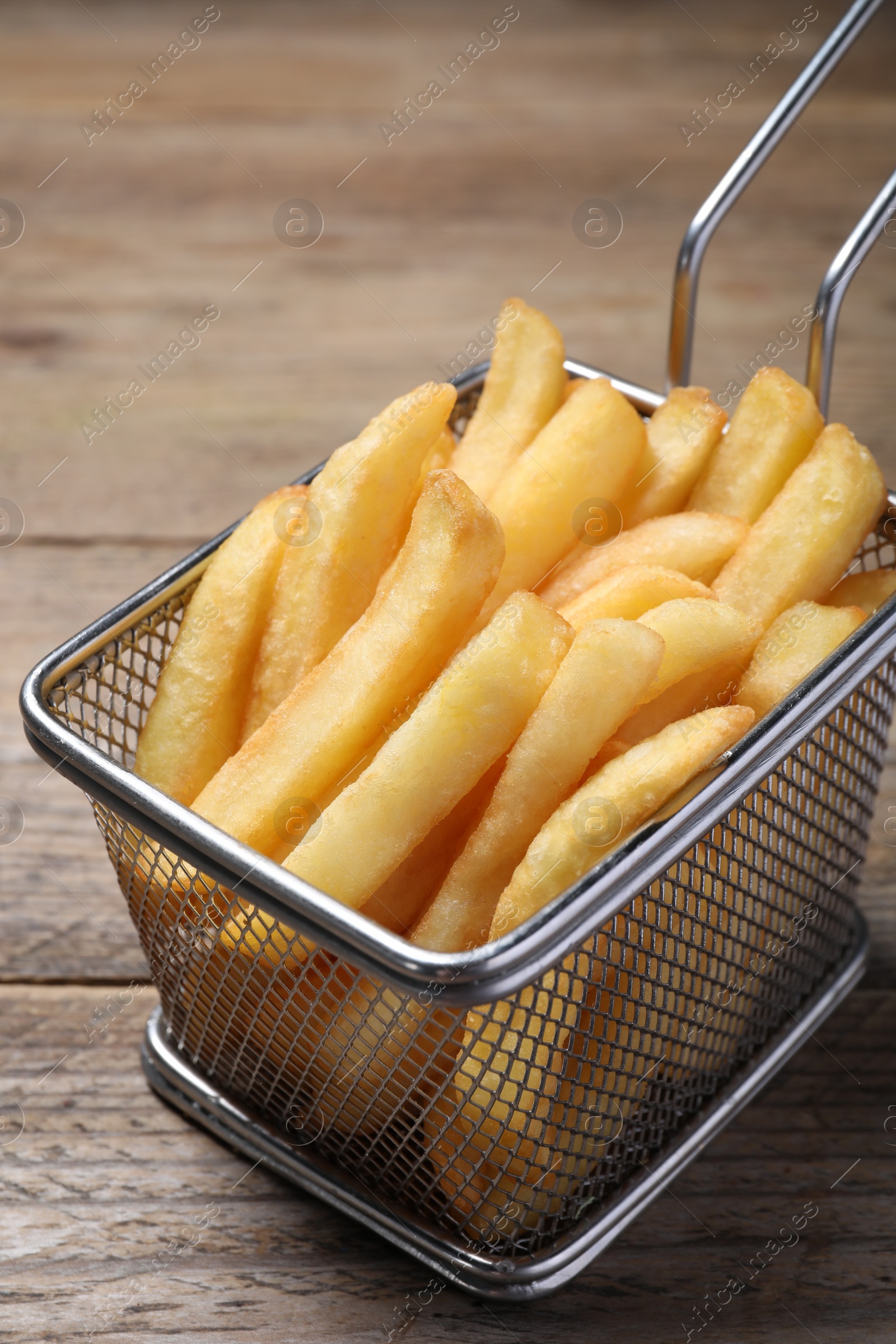 Photo of Tasty French fries in metal basket on wooden table, closeup