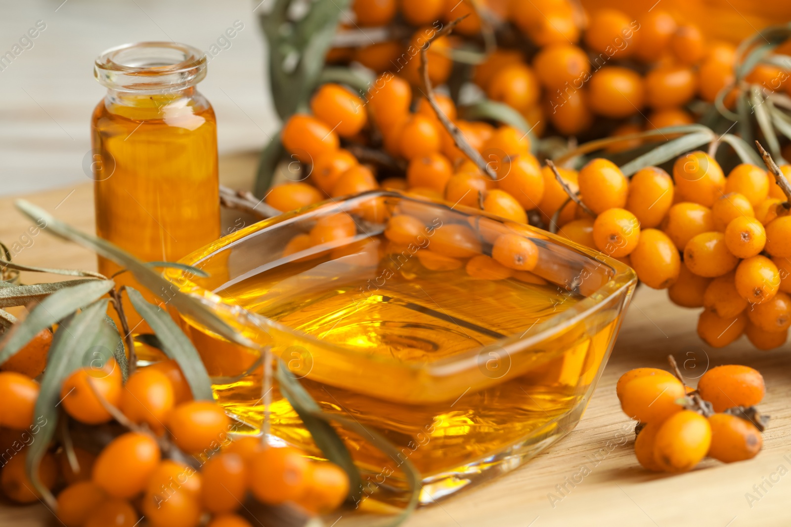 Photo of Natural sea buckthorn oil and fresh berries on wooden table, closeup