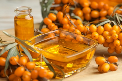 Natural sea buckthorn oil and fresh berries on wooden table, closeup