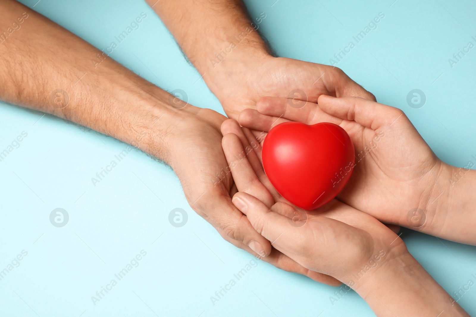 Photo of Couple holding red heart in hands on light blue background, closeup