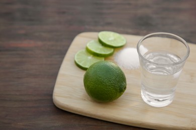 Photo of Mexican tequila shot with lime slices on wooden table, closeup and space for text. Drink made from agave