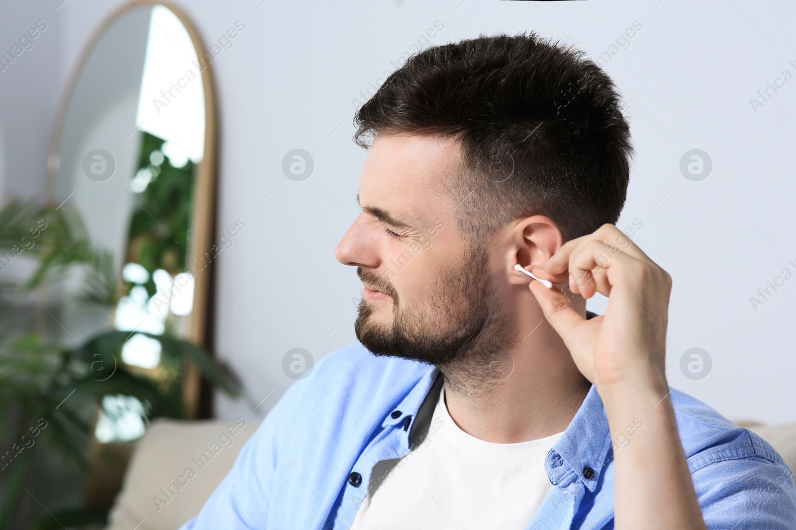 Photo of Young man cleaning ear with cotton swab at home. Space for text