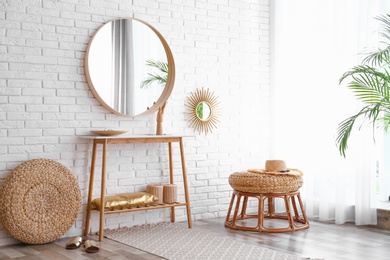 Hallway interior with big round mirror, table and decor near brick wall