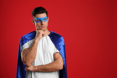 Man wearing superhero cape and mask on red background. Space for text
