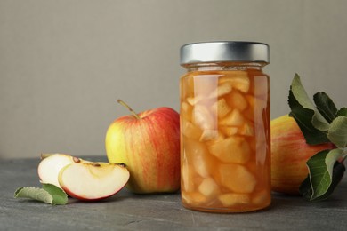 Photo of Tasty apple jam in glass jar and fresh fruits on grey table, space for text