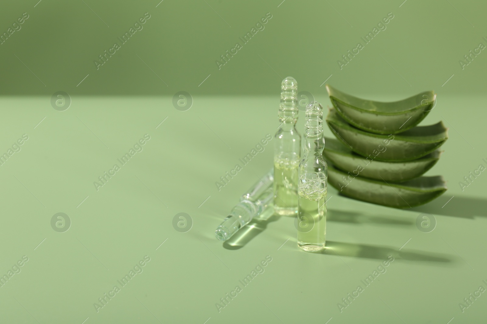 Photo of Skincare ampoules with extract of aloe vera and cut leaves on pale green background. Space for text