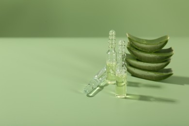 Skincare ampoules with extract of aloe vera and cut leaves on pale green background. Space for text