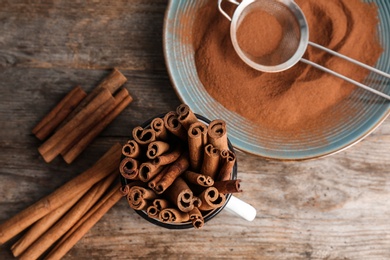 Mug with aromatic cinnamon sticks and powder on wooden background