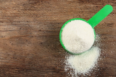 Photo of Measuring scoop of protein powder on wooden table, top view. Space for text