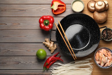 Black wok and chopsticks surrounded by products on color wooden table, flat lay. Space for text