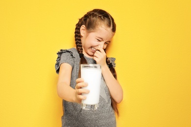 Little girl with dairy allergy holding glass of milk on color background