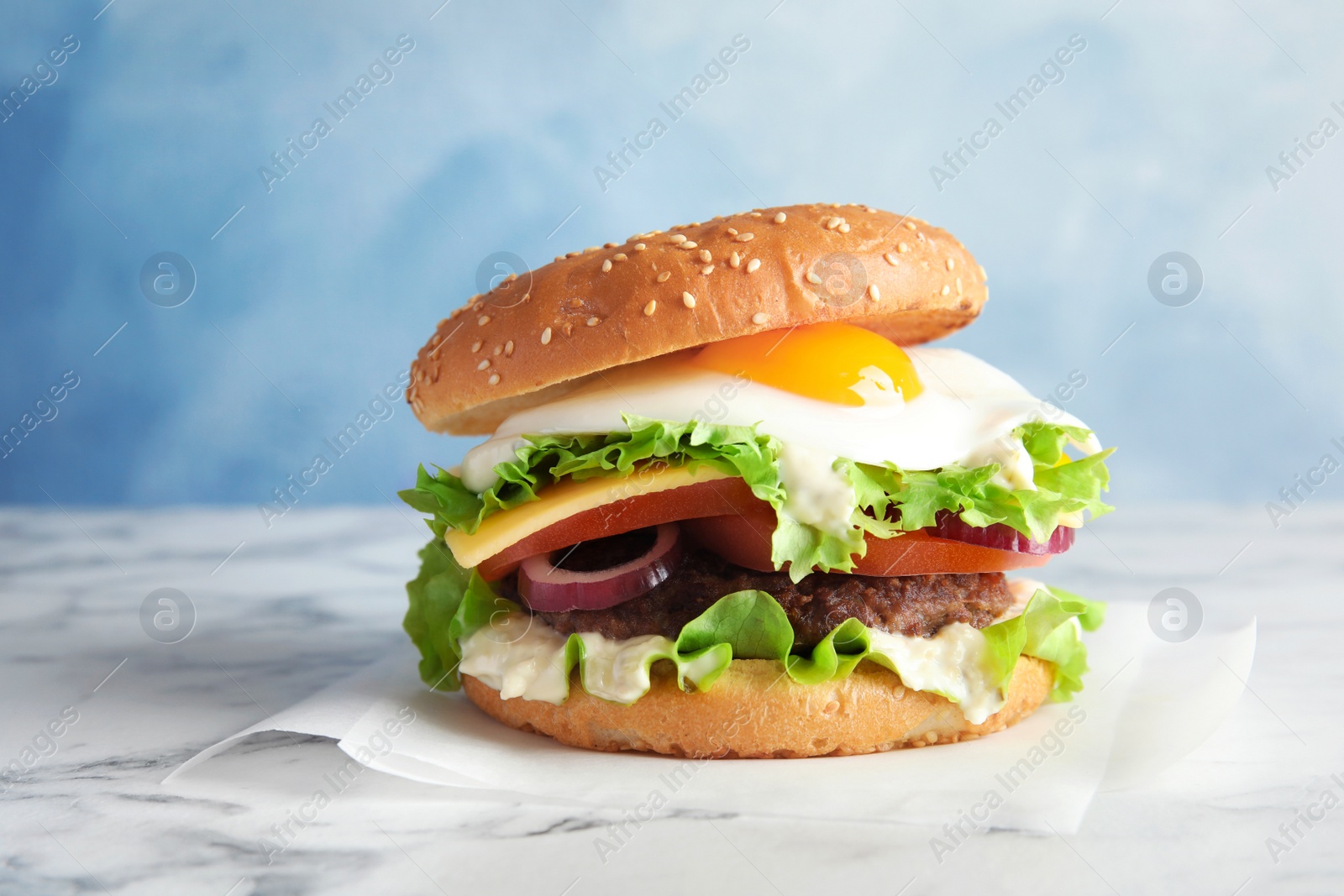 Photo of Tasty burger with fried egg on marble table against color background