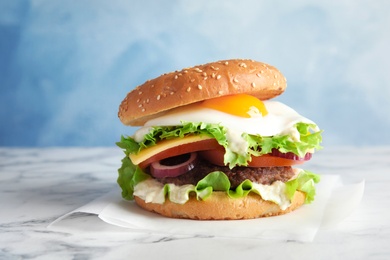 Tasty burger with fried egg on marble table against color background