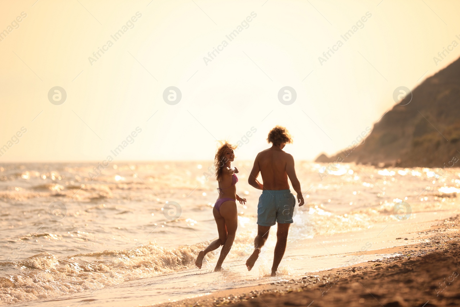 Photo of Young woman in bikini and her boyfriend having fun on beach at sunset. Lovely couple
