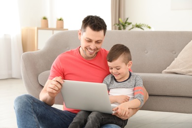 Boy and his father with laptop sitting near the sofa on floor. Family time