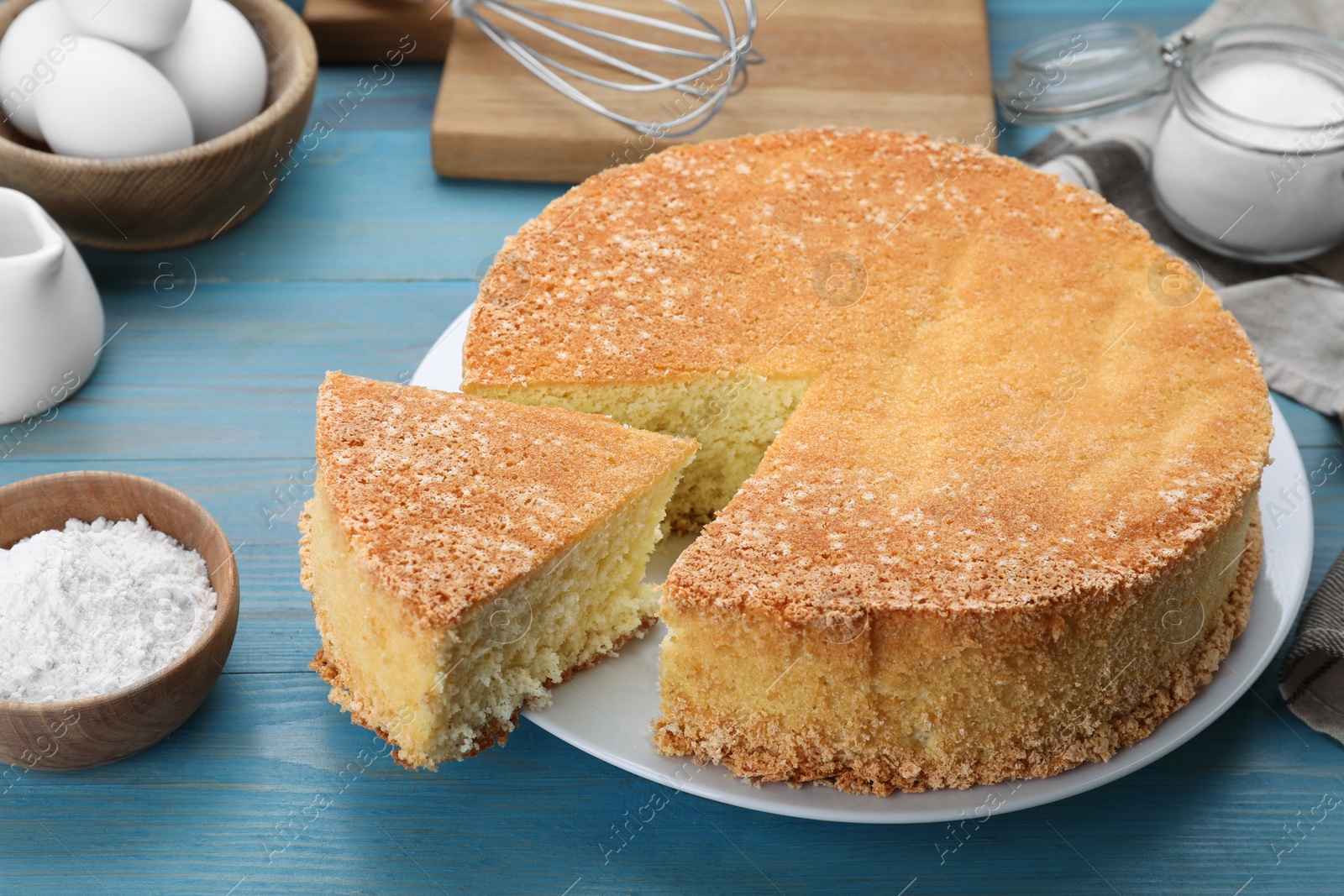 Photo of Tasty sponge cake and ingredients on light blue wooden table