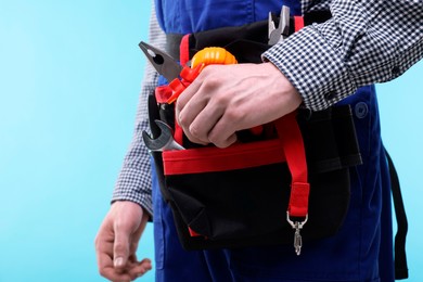 Photo of Young man with pliers and other tools in bag on light blue background, closeup