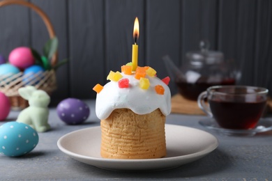 Photo of Traditional Easter cake with burning candle on grey wooden table