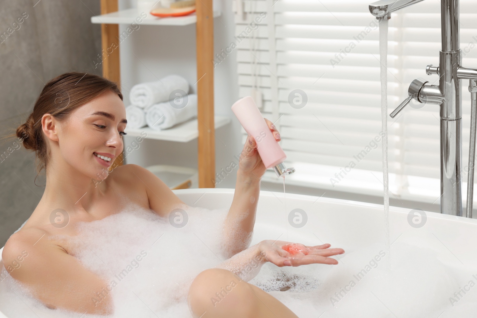 Photo of Woman pouring shower gel onto hand in bath indoors