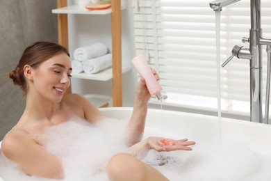 Photo of Woman pouring shower gel onto hand in bath indoors