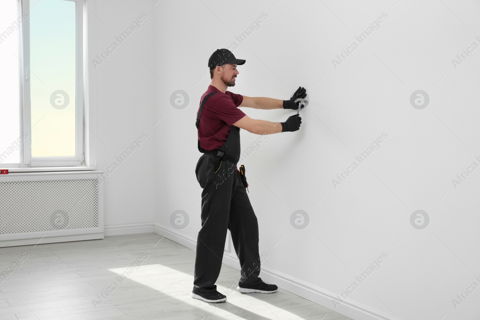 Photo of Handyman in uniform working with hammer indoors. Professional construction tools