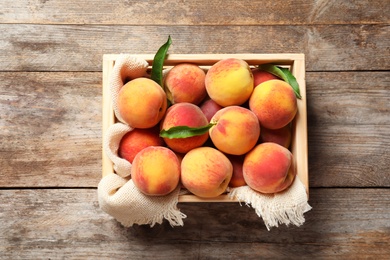 Photo of Wooden crate with fresh sweet peaches on table, top view